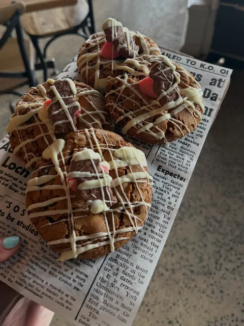 Cookies drizzled with white chocolate and topped with chocolate figures, on newspaper-print paper